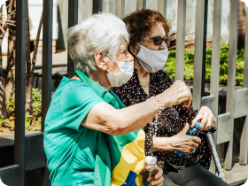a couple of older women with masks sitting and waiting by the bus stop
