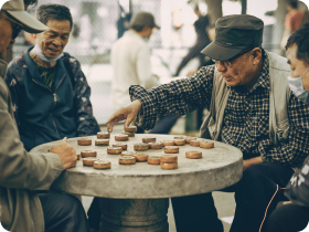 small group of elderly asian men playing chinese chess outside at the circular stone tables