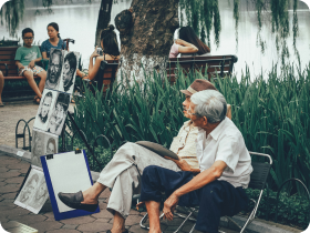 two elderly men sitting y a lake near some younger kids